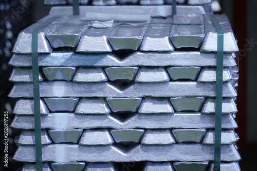 A neat stack of raw aluminum ingots bound with green plastic strapping inside an industrial foundry warehouse.