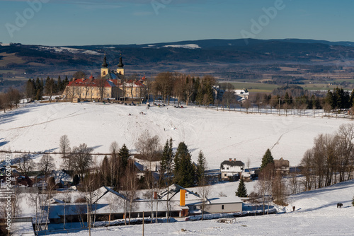 A scenic winter landscape capturing the historic Monastery of the Mother of God (Klaster Hedec) on a snowy hill near Kraliky, East Bohemia, Czechia. Sunny winter day with white snow covering fields an