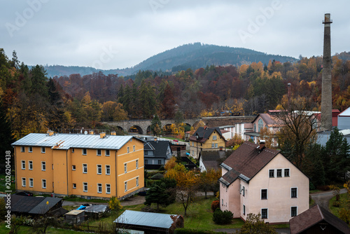 Scenic valley view of Desna town with historic railway viaduct and factory chimney in autumn Jizera Mountains