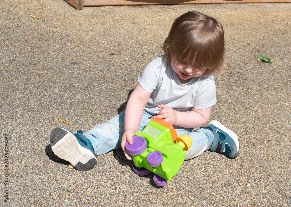 Naklejka premium Adorable toddler boy playing with colorful toy train on playground outdoors