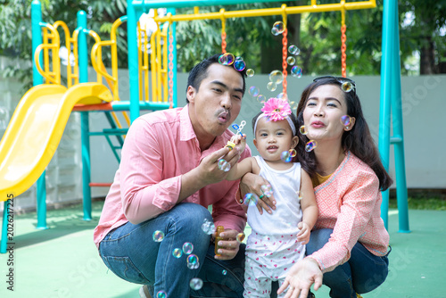 Asian Parents Blowing Soap Bubbles for Young Daughter at Colorful Playground
