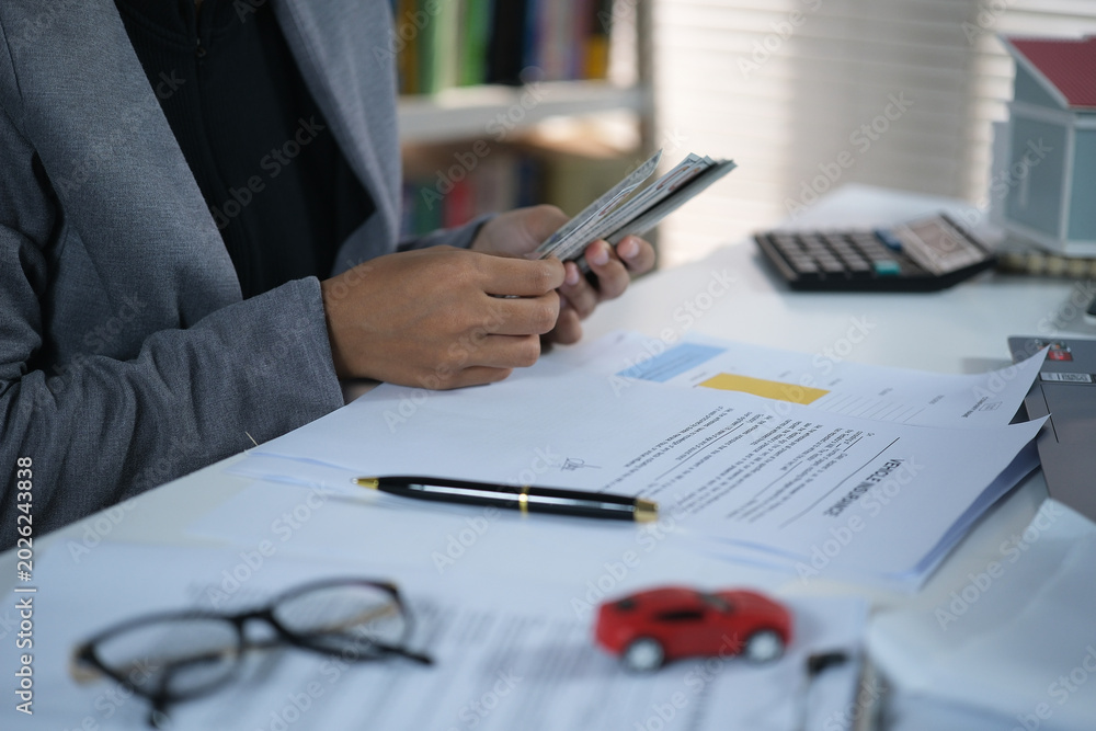 Fototapeta premium Bussines woman counts dollar bills with a miniature red car on his desk, The concept of installment payments, rent, buying and selling, insurance and vehicle tax. 
