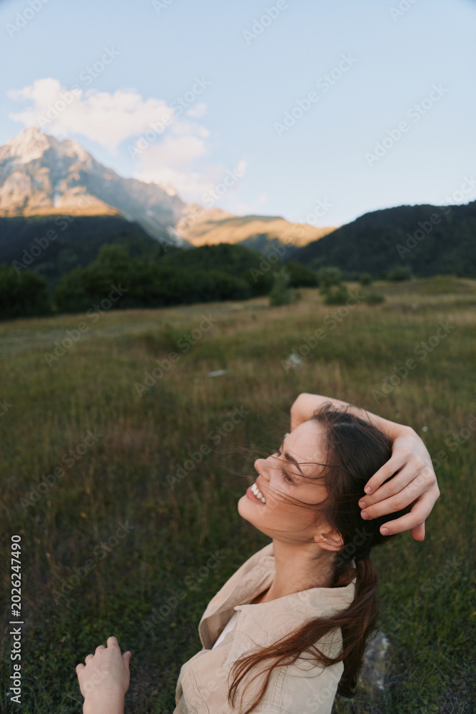 Fototapeta premium Joyful woman outdoors in a meadow, enjoying sunlight, laughter, and a gentle breeze with mountains in the distance, a serene lifestyle moment in nature