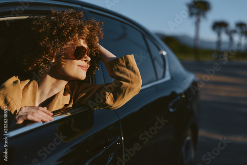 Foto Woman leaning from a glossy car window, basking in sunlit breeze, casual lifesty