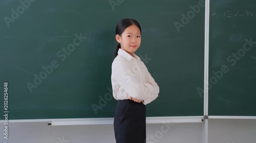 Confident Asian Schoolgirl Standing in Front of Blackboard with Folded Arms
