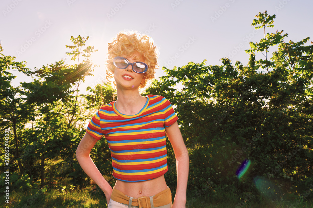 Fototapeta premium Cheerful woman outdoors, sunglasses and striped crop top, sunlit moment with a bright smile, casual pose under warm breeze, vibrant nature and retro film color mood