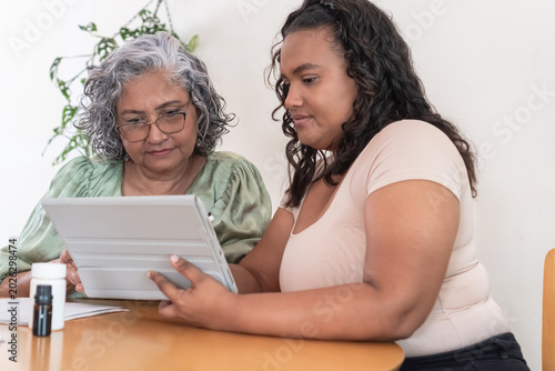 Fotografie Caregiver assisting elderly woman learning technology on tablet