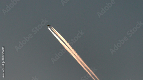 Foto Minimalist view of a commercial jet airplane flying at high altitude leaving long contrails illuminated by warm golden hour sunlight against a moody sky