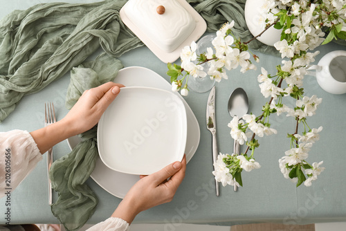 Foto Woman setting table with beautiful blossoming branches, plates, glass and fabric