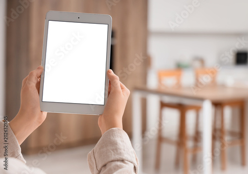 Young woman holding modern tablet computer with blank screen at home, closeup
