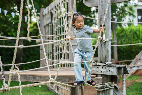 preschool child girl playing and walking on wooden rope bridge at outdoor playground in park