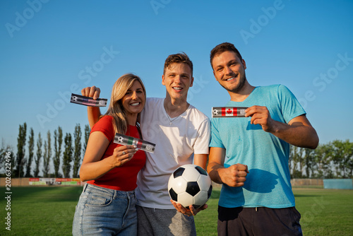 Group of three friends, two guys and a girl holding tickets for soccer match, on tickets are flags of Mexico, Canada and USA
