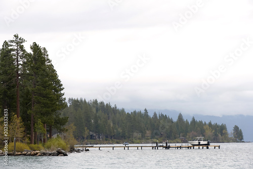 Pine trees along South Lake Tahoe with a small pier out into the water, a white boat docked in the bay.