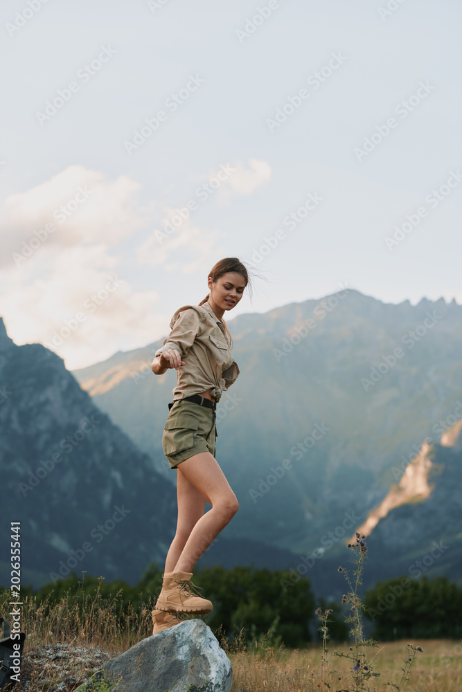 Fototapeta premium Vibrant woman enjoying the outdoors in a mountain landscape, smiling with relaxed posture, sunlit breeze, casual outfit, natural colors, scenic terrain, carefree mood