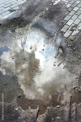 The reflection of cloud cover on the surface of a mud puddle in an outdoor area