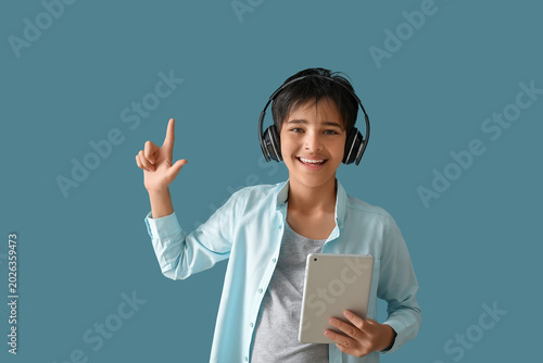 Little boy in headphones with tablet computer pointing at something on blue b...