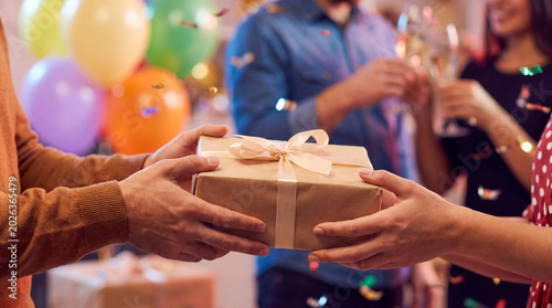 Obraz na płótnie Hands exchanging a gift box at a festive party with balloons.