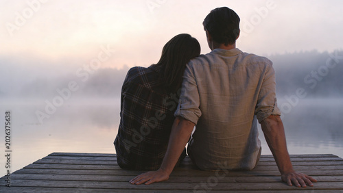 Couple sitting on a wooden dock overlooking a misty lake at sunrise