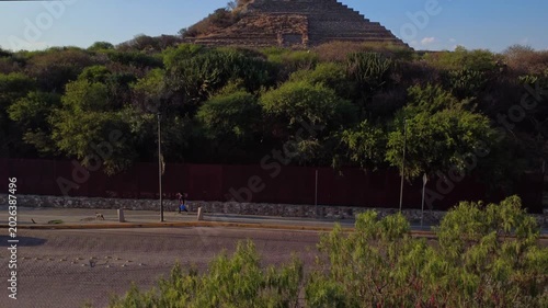 Aerial tilt up shot revealing ancient Mesoamerican pyramid in Querétaro Mexico surrounded by urban landscape at golden hour with dramatic skyline and mountains in background