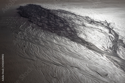 Tidal water patterns and sand ripples form intricate natural textures on a beach at low tide
