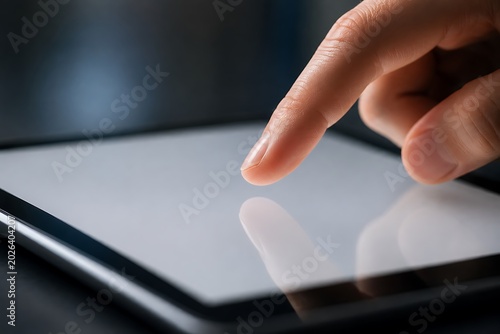 A close-up shot of a person's finger touching the screen of a tablet device.