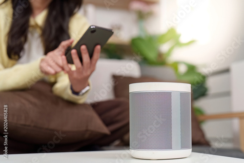 Asian woman using smartphone with smart speaker in modern home
