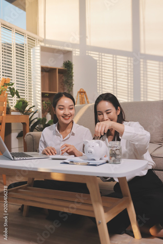 Happy asian young couple love hand calculate, putting coin in piggy bank for saving money to buy real estate for new home. Business finance, deposit with banking for financial planning future together