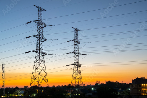 Foto Power Lines at Dusk: Towering electricity pylons stand silhouetted against a vibrant twilight sky, casting long shadows over a darkened landscape as the day gives way to night