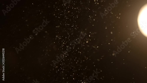 Floating dust particles illuminated by bright light in dark room.