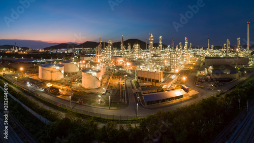 Schilderij op canvas Industrial Complex at Dusk: An expansive oil refinery complex glows with illuminated pipes and towering structures against a twilight sky, signifying heavy industry and energy production