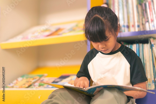 Child reads book in library with colorful shelves during daytime in a quiet learning space