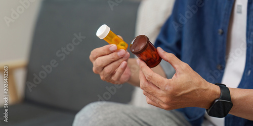 Asian senior man patient holding medication pill bottles at home