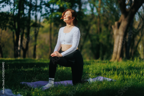 Photography Mature woman doing fitness meditating with closed eyes in sunny forest park