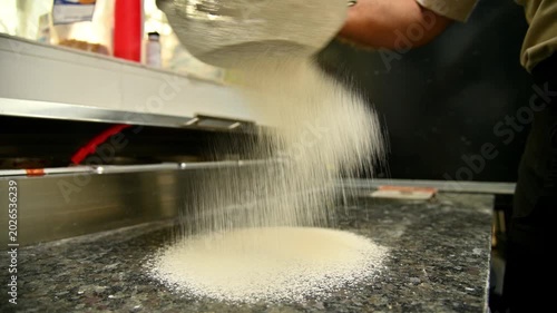 Man sifts flour from a bowl onto a granite countertop in a kitchen setting