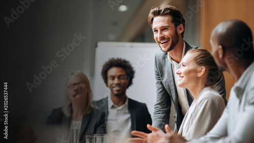 Group of diverse professionals engaged in lively business meeting, with focus on smiling man leading discussion. atmosphere is collaborative and positive