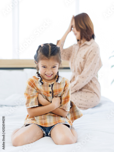 Quadro su tela Asian unhappy daughter feeling sad sulking her mothers sitting on bed, mom talk to ignorant stubborn little child girl avoid communication misunderstanding generation gap family conflicts problems