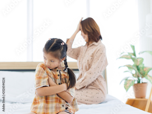Quadro su tela Asian unhappy daughter feeling sad sulking her mothers sitting on bed, mom talk to ignorant stubborn little child girl avoid communication misunderstanding generation gap family conflicts problems