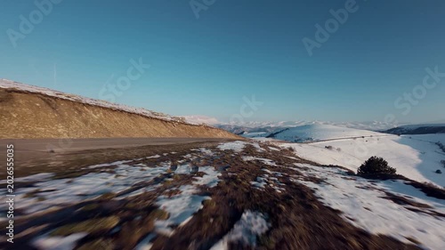 FPV low flight over snowy hillside and winding road in mountainous landscape