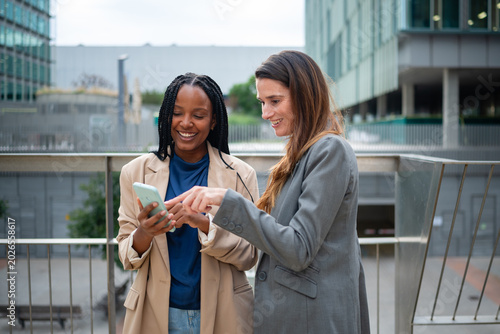 Two diverse businesswomen collaborating using smartphone technology