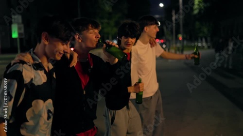 Four excited teenage boys shouting and drinking beer on a city street at night.
