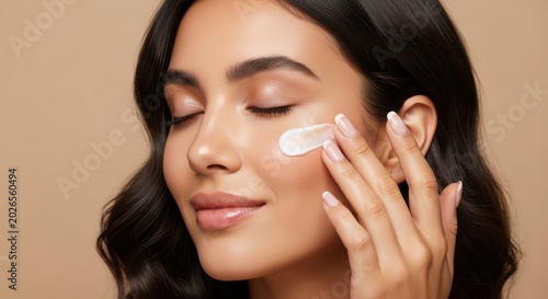 Woman applying cream to her face with her fingers on a beige background