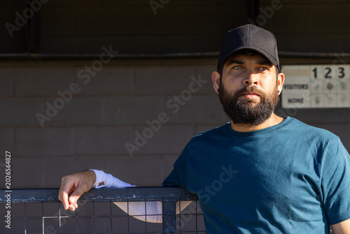 Cuadro en lienzo Man leaning on chain-link fence in dugout wearing teal T-shirt, black cap, copy