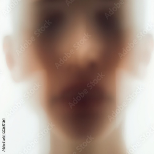 An abstract and mysterious close-up portrait shows the heavily blurred motion silhouette of a person's lips and nose fading into a bright white background.