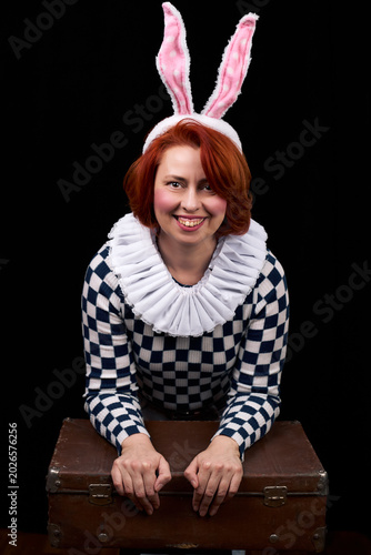 Smiling woman wearing bunny ears leaning on vintage suitcase in studio