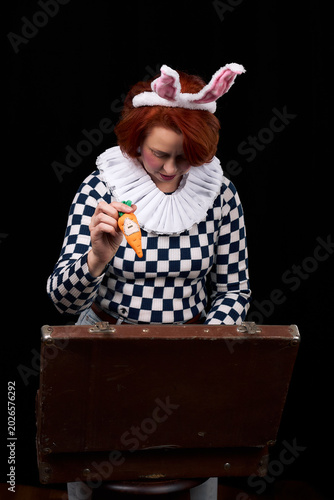 Woman with bunny ears holding carrot toy looking into vintage suitcase