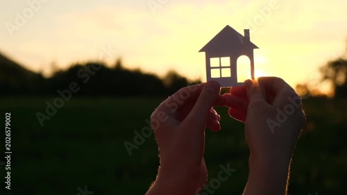 Child hands holding paper house standing in fields at amazing sunset sun village. Preteen girl hold home model dream buying real estate investment mortgage bank loan insurance concept