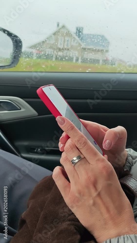 Close-up of neatly manicured woman hands texting and watching content on smartphone as car passenger. Vertical 4K footage.