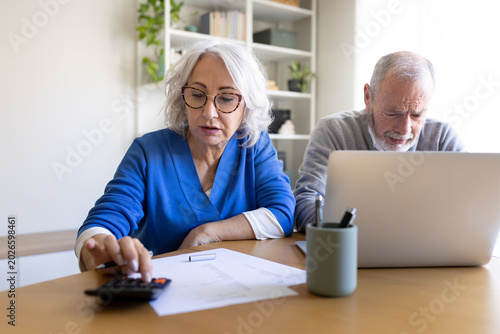 Senior couple managing domestic finances with laptop and calculator at home