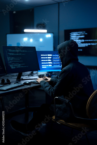 Foto Male computer hacker in black hoodie typing code on computer in a dark room with light reflection on glasses