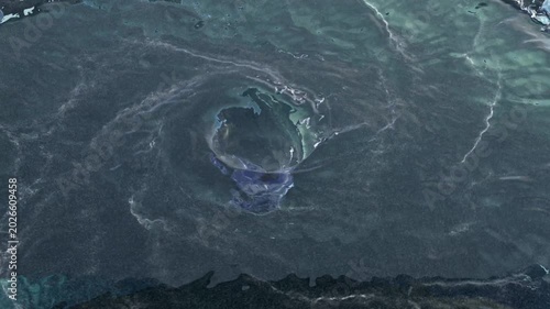 Aerial view of a water vortex turning fast with turbulences and the end of a hole in the center on a dark floor